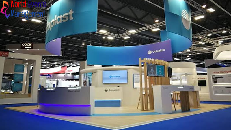 Large blue exhibition stand with curved hanging banner, digital displays, and open booth layout
