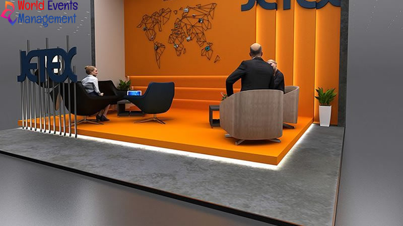 Orange themed exhibition stand with reception counter and seating area